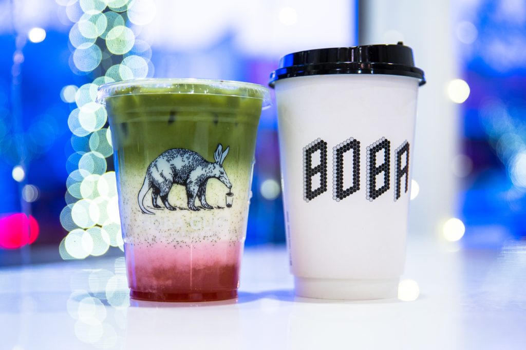 A plastic cup filled with boba tea, and a coffee cup with the word Boba on the side.