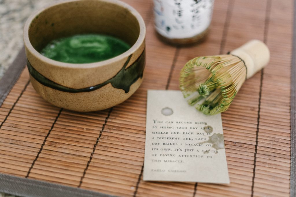 A cup of matcha green tea and a bamboo matcha whisk