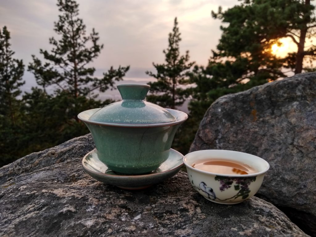 A Chinese teapot beside a cup of tea on a rock on a mountain
