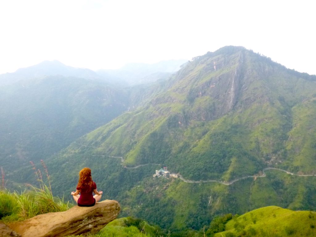 A woman sitting on a ledge in front of a mountain in Sri Lanka, meditating. 
